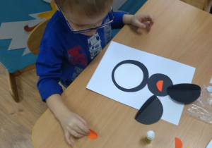Chłopczyk przykleja na karton elementy pingwinka.